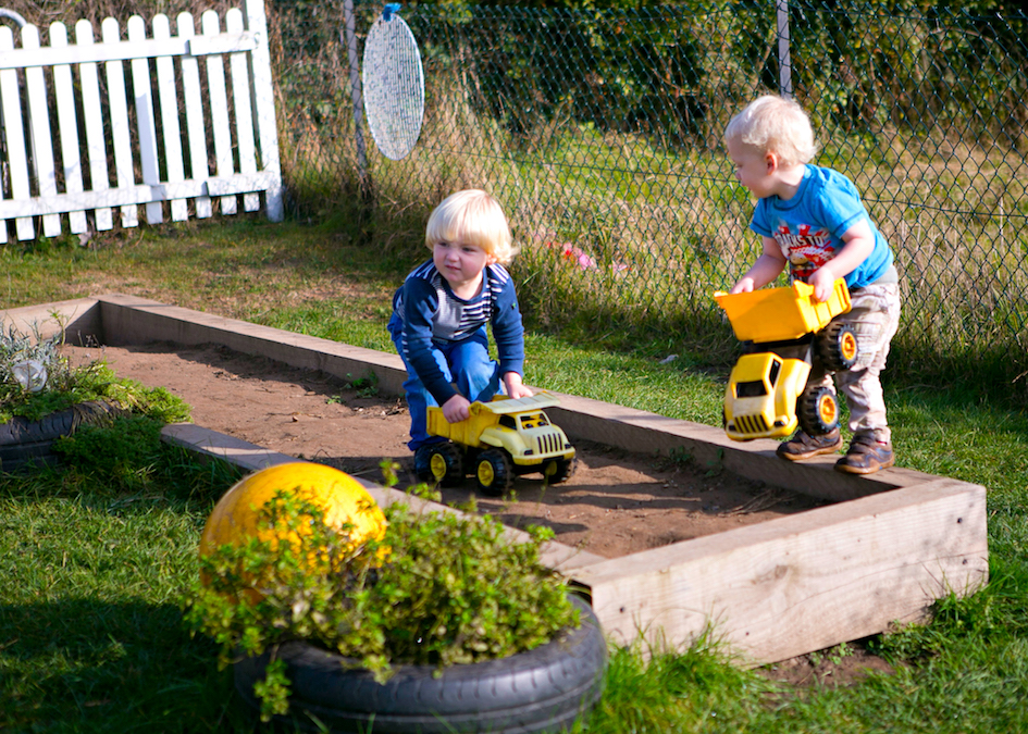 Children playing with yellow trucks in the garden.
